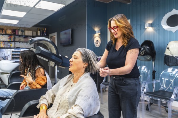 Professional hairdresser washing and styling a smiling mature womans gray hair in a modern salon,