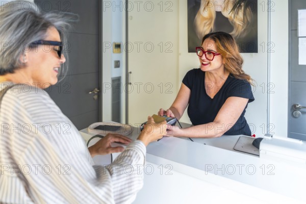 Senior customer making a contactless credit card payment at the reception desk to a smiling female