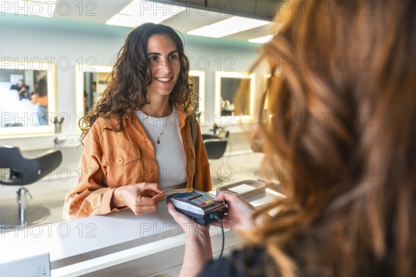 Smiling woman paying with a contactless credit card at a modern hair salon reception, completing a