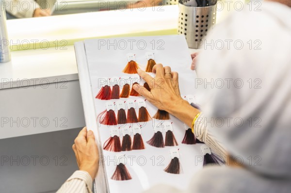 Client selecting desired hair dye shade from a detailed color chart while sitting in a hair salon,