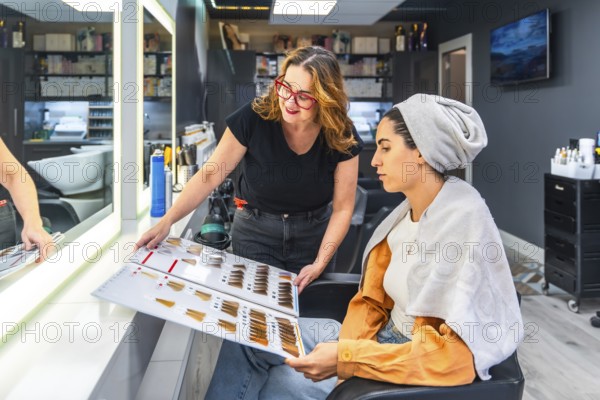 Professional hairstylist assisting a young woman in choosing the perfect hair dye shade from a