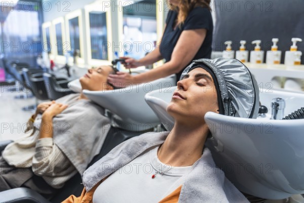 Woman relaxing with eyes closed while receiving a hair treatment and shampoo service at a beauty