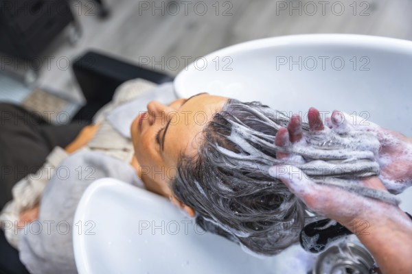 Mature woman relaxing with eyes closed as a hairdresser shampoos her long dark hair over a salon