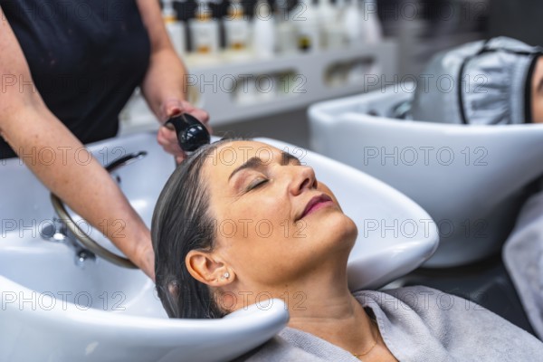 Woman with closed eyes relaxing during a hair wash service at a beauty salon, symbolizing self