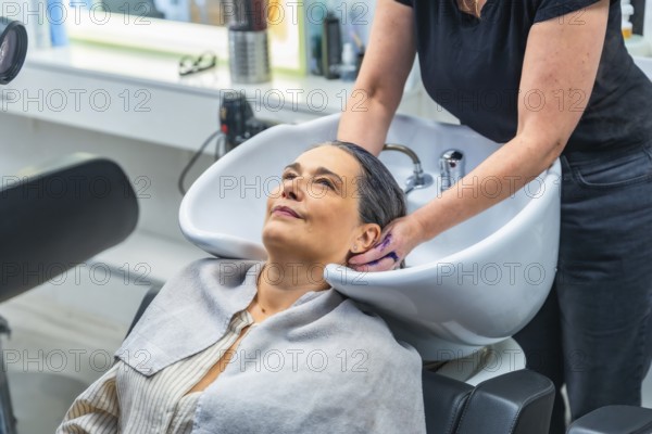 Senior woman smiling as a hairstylist gently washes her hair at a modern salon basin, enjoying a