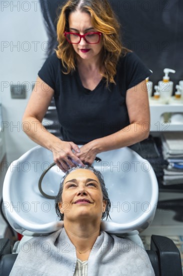 Hair stylist washing a mature woman's hair at the shampoo sink, creating a moment of self care,