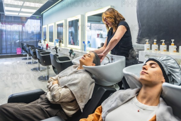 Hairdresser washing client's hair at a modern salon basin, two women enjoying a relaxing,