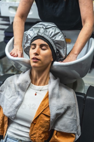 Relaxing woman with eyes closed wearing a heat cap during a professional hair treatment at a modern
