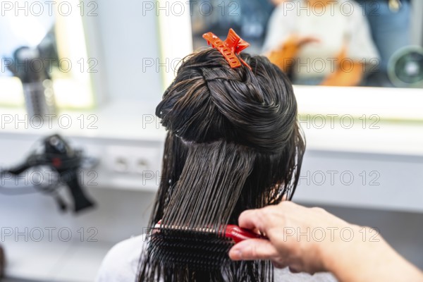 Hairdresser's hand brushing through long, wet hair of a woman, carefully sectioning strands with