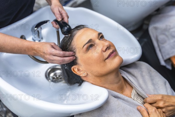 Senior woman smiling as a professional hairdresser washes and massages her hair at a salon sink,