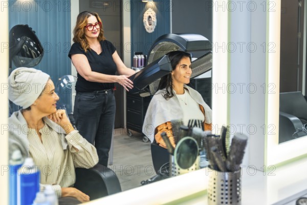 Hairdresser working on a client's hair with a professional bonnet dryer in a modern salon while