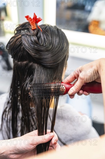 Hairdresser performing a hair styling service on a female client, brushing her wet dark hair after