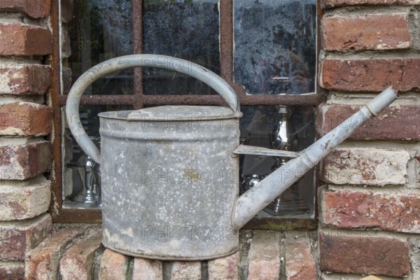 Old metal watering can on a brick window sill in front of a rusted lattice window, North