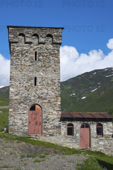 Old stone tower and small building against a mountain backdrop under a deep blue sky, defensive