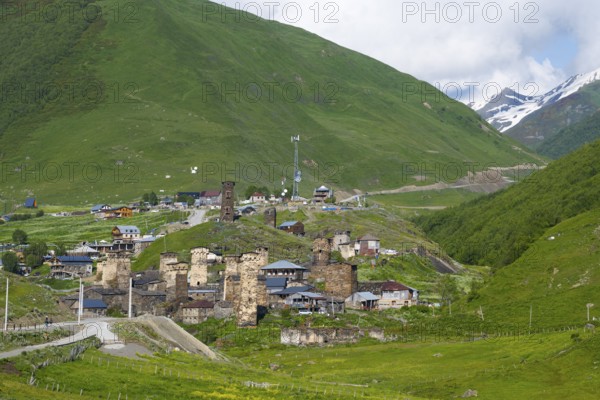 Mountain village with old stone towers surrounded by green hills and mountains under a partly