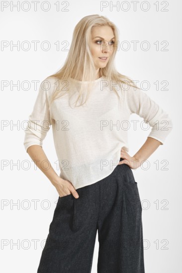 A woman stands confidently with one hand on her waist. They wear a light top and dark,