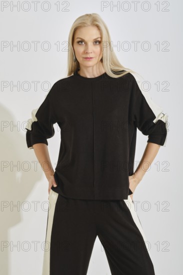 A woman stands with a confident pose wearing a comfortable black tracksuit with white stripes on