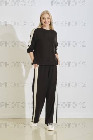 A woman stands confidently in a black and white athletic outfit with pockets, showcasing a modern