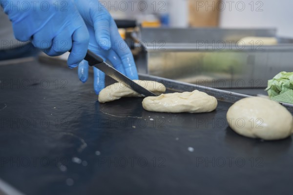A baker shapes and cuts dough with a knife on a black surface, bake rolls, Haselstaller Hof,