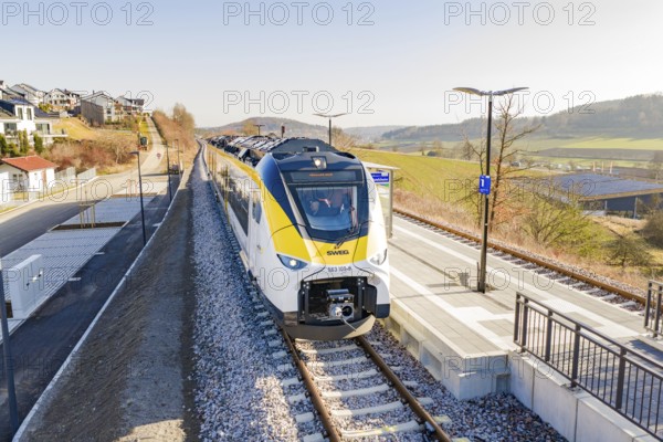 Modern train at the station, surrounded by rural architecture and extensive landscape, test run on