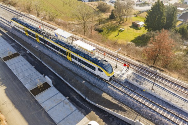 Train at train station surrounded by people, landscape with fields and trees, test run on the new