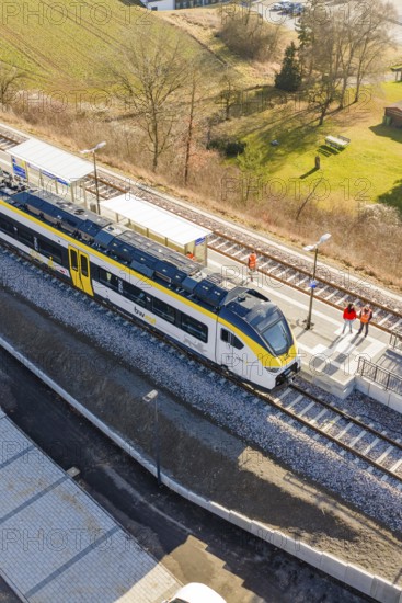 A train is standing on the platform, people on the track, surrounded by fields and countryside,