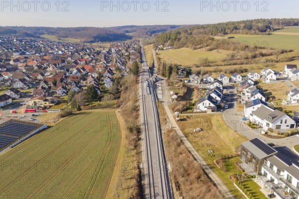 Railway tracks cross an extensive landscape with houses and fields, aerial view, test run on the