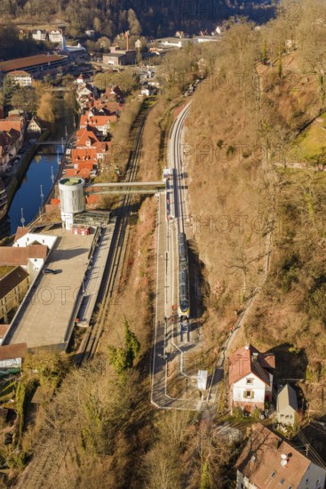 Train travels through a hilly landscape with village and river from a bird's eye view, test trip on
