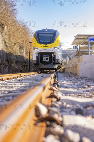 Close-up of a yellow and white train on gravel tracks at a bus stop, test run on the new