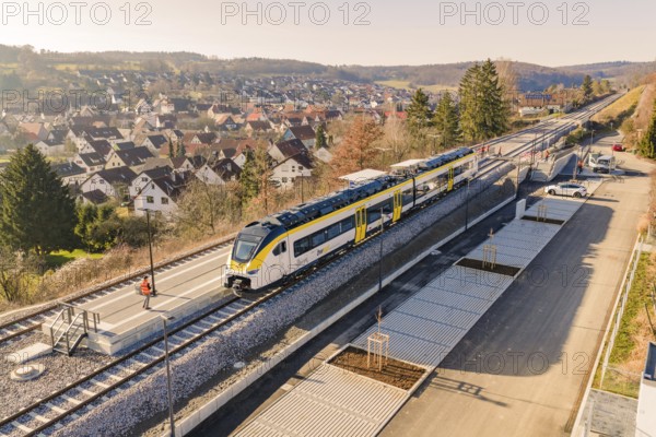Train at a train station in a rural area surrounded by hills and houses, test ride on the new