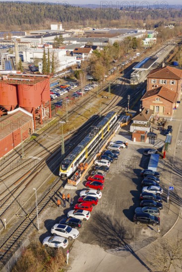 Train in a train station with adjacent parking lot and buildings in an industrial area, test run on