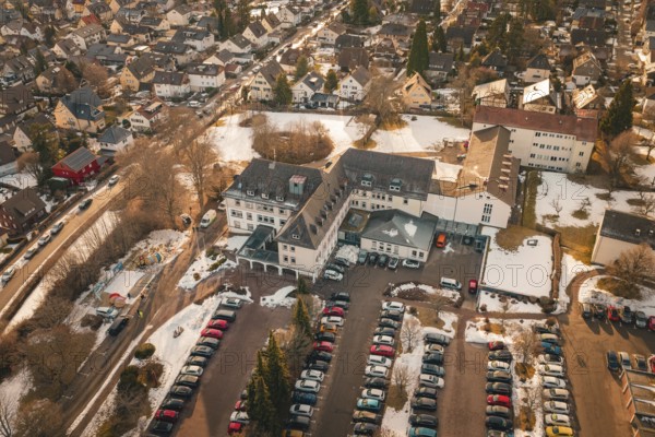 View of a large building complex with parking spaces and surrounding residential area in winter,