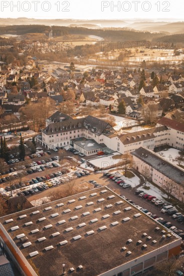 Aerial view of a city with many buildings, warm sunlight, parked cars and winter landscape,