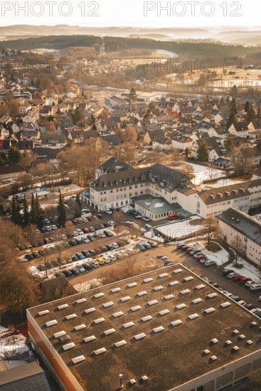 Urban area in winter with snow-covered houses and roads in warm sunlight from a bird's eye view,