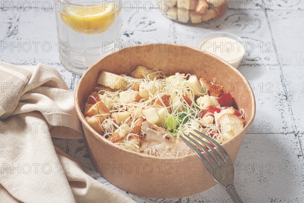 Caesar salad in a paper container, take it on the way, with sauce and croutons, on the table,
