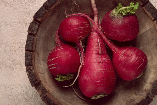 A collection of vibrant red radishes sits in a round wooden bowl, showcasing their natural texture