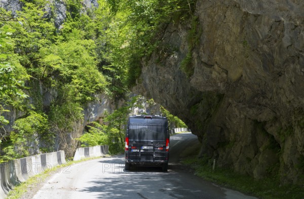 A black van drives on a narrow mountain road surrounded by lush greenery, camper, motorhome in a