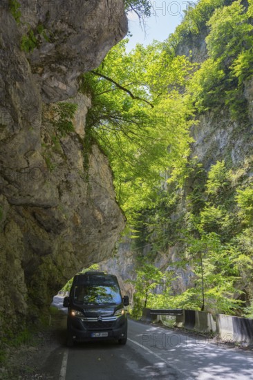A black van drives along a shady mountain road lined with rocks and trees, camper, motorhome in a