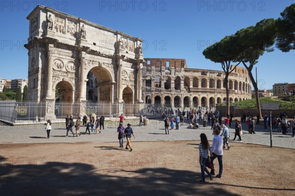 Arch of Constantine and Colosseum surrounded by tourists under blue sky and green grass, Rome,