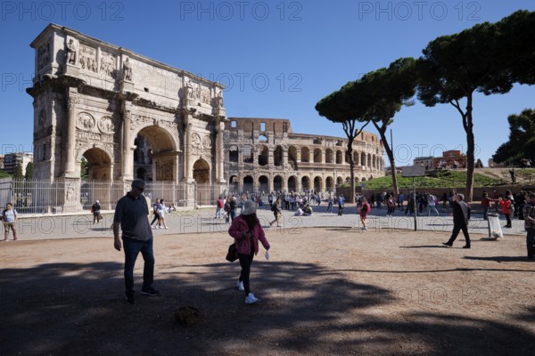 Tourists in front of the Colosseum and Arch of Constantine on a sunny day surrounded by trees,