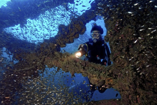 Underwater photo diver dives through parts of former sunken tin excavator Boonsung wreck off the