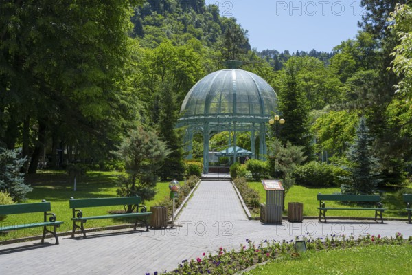 A path through a green park leads to a pavilion surrounded by flowers and trees, pavilion with