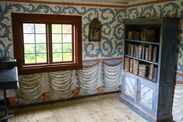 Small room with an antique bookshelf and artfully decorated walls next to a window in the