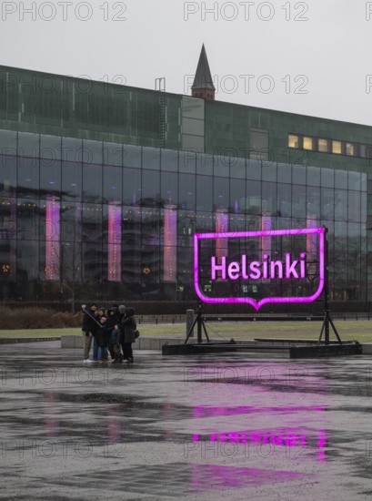 Tourists with selfie sticks take pictures of themselves in front of the glowing pink Helsinki city