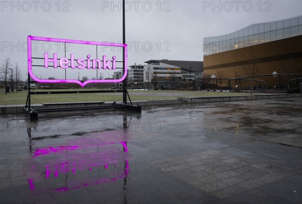Large pink glowing Helsinki city logo, in front of Oodi Central Library and Cultural Center,