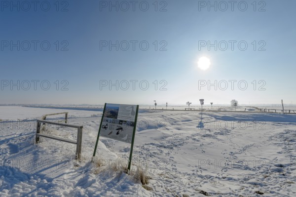 Snowy landscape with information board under bright blue sky in the Ochsenmoor nature reserve area,