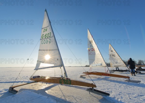 Three ice sailboats on frozen lake under clear blue sky and bright sunshine on frozen Dümmer,