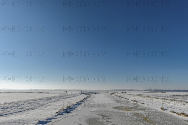 Snowy open landscape with wide sky and distant horizon under blue sky in the foreground the frozen