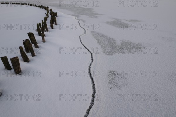 Frozen lake surface of Dümmer See with wooden posts and distinctive fault line in ice, frozen