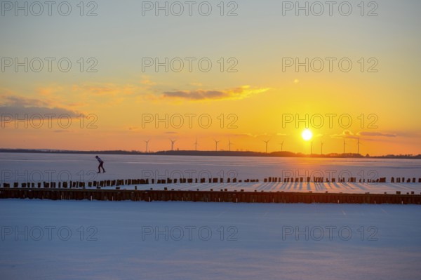 Ice skaters in front of sunset over icy landscape with wind turbines and intense colors on the